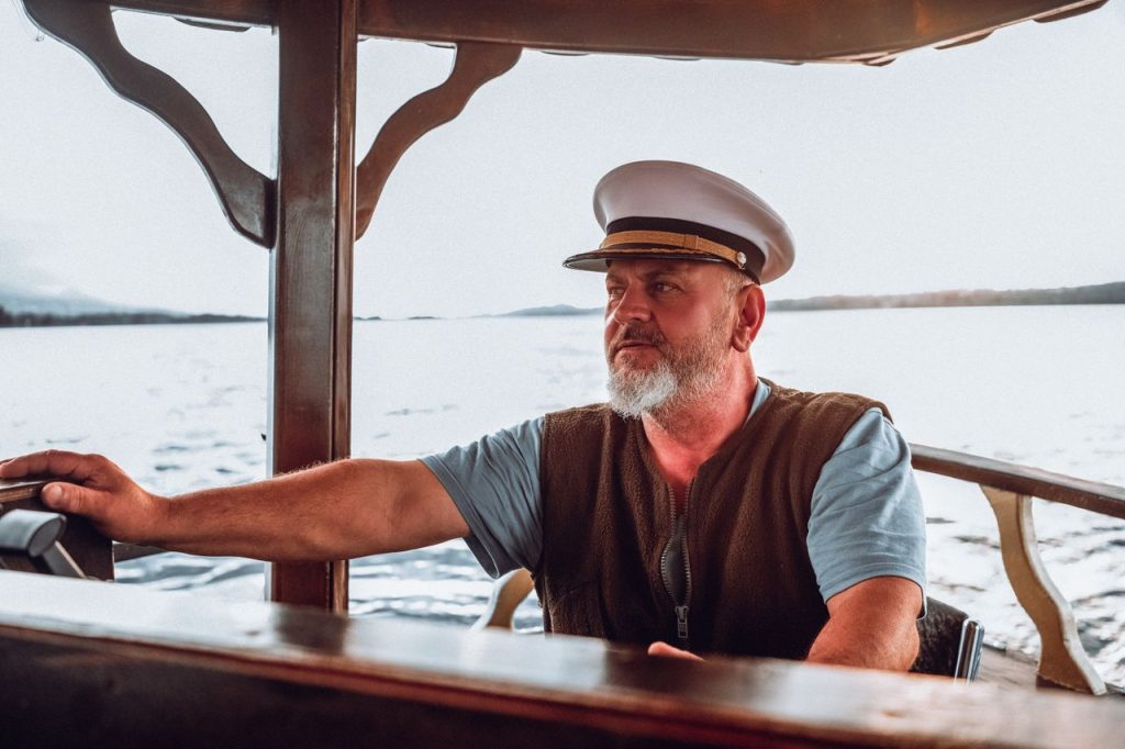 An elderly man steering a boat on a sunny day, showcasing maritime expertise and leadership.